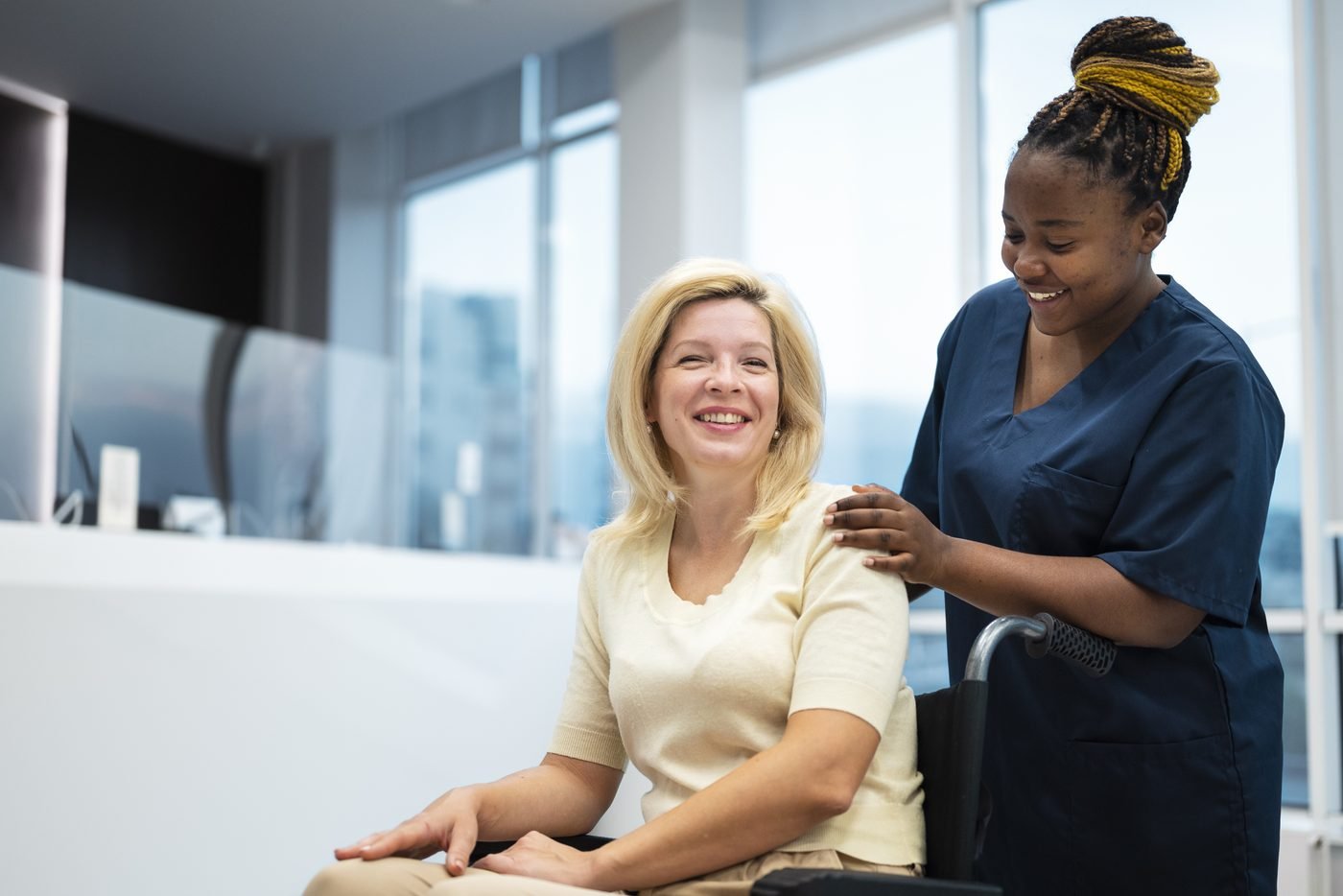 A smiling care worker resting a supportive hand on the shoulder of a woman using a wheelchair